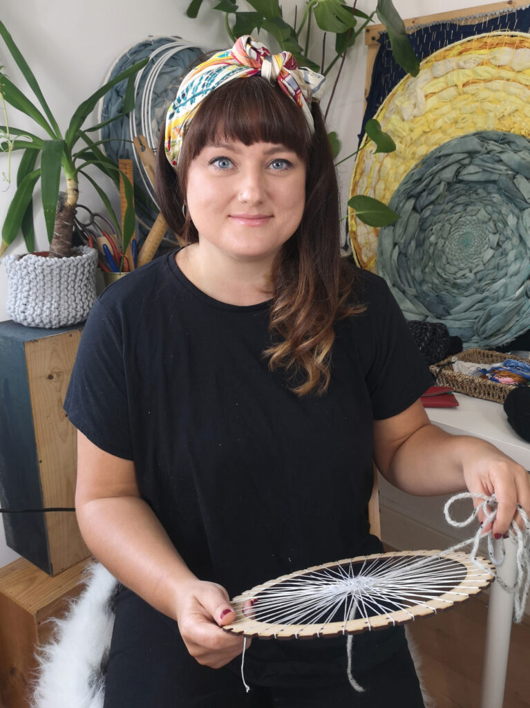 Laura Segan is a mixed-media artist and art therapist. Here she is seen weaving a piece of art with more of her artwork in the background.
