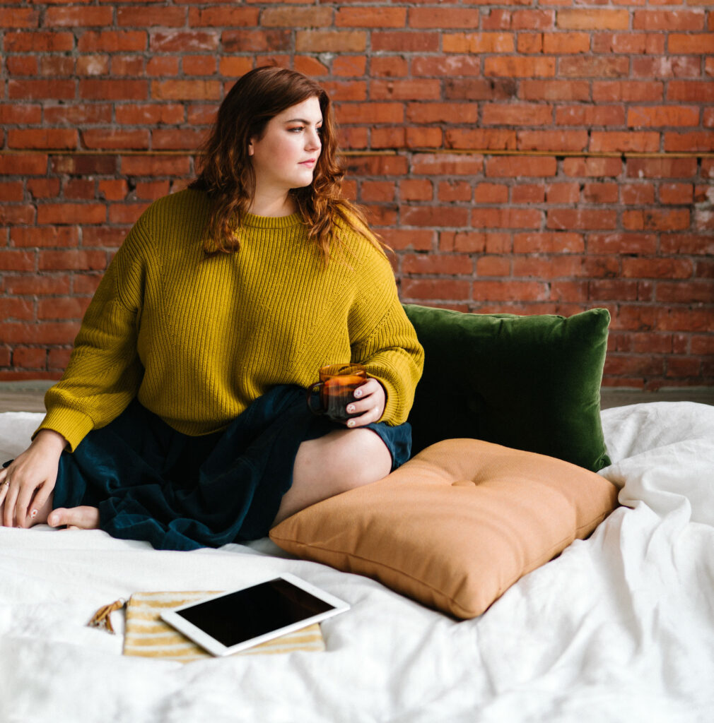 How to overcome crippling self doubt in business. A woman sits on a bed in front of a red brick wall.
