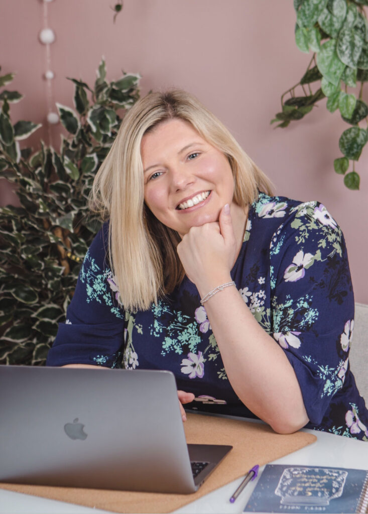 Lucy Linn of Empower coaching and consultancy sat smiling at her laptop in a pink office